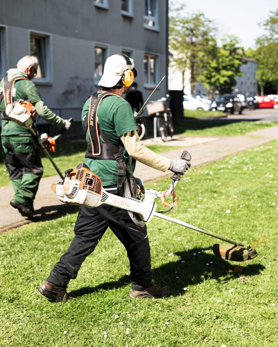 Rohfoto vom Drehtag: Mitarbeiter in der Grünpflege vor einer Wohnanlage