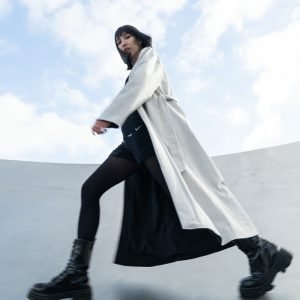 Fashion-Shooting, Model im weissen Mantel in Bewegung vor Beton und Himmel